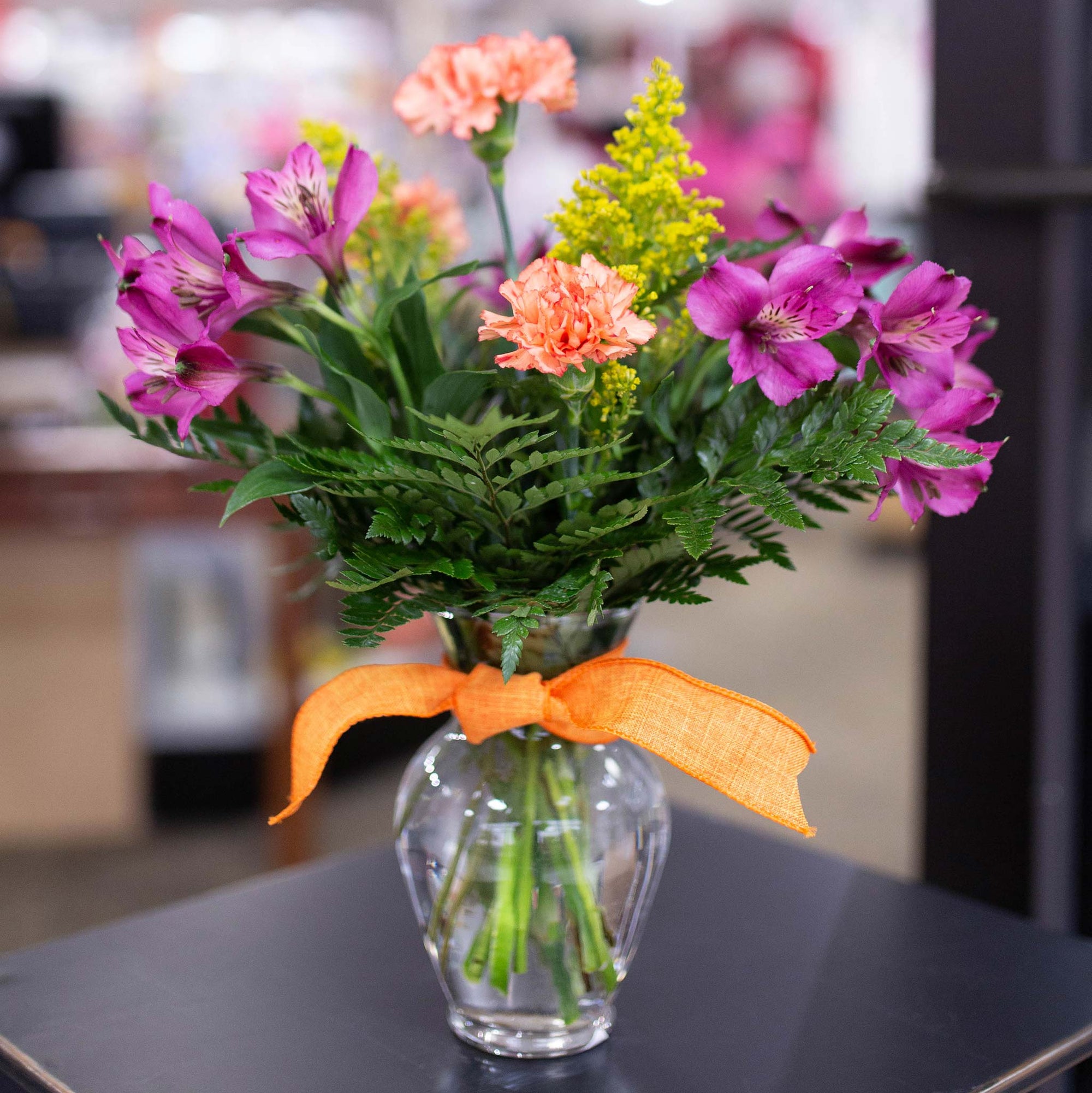 Orange carnations and purple and yellow flowers in a vase with ribbon